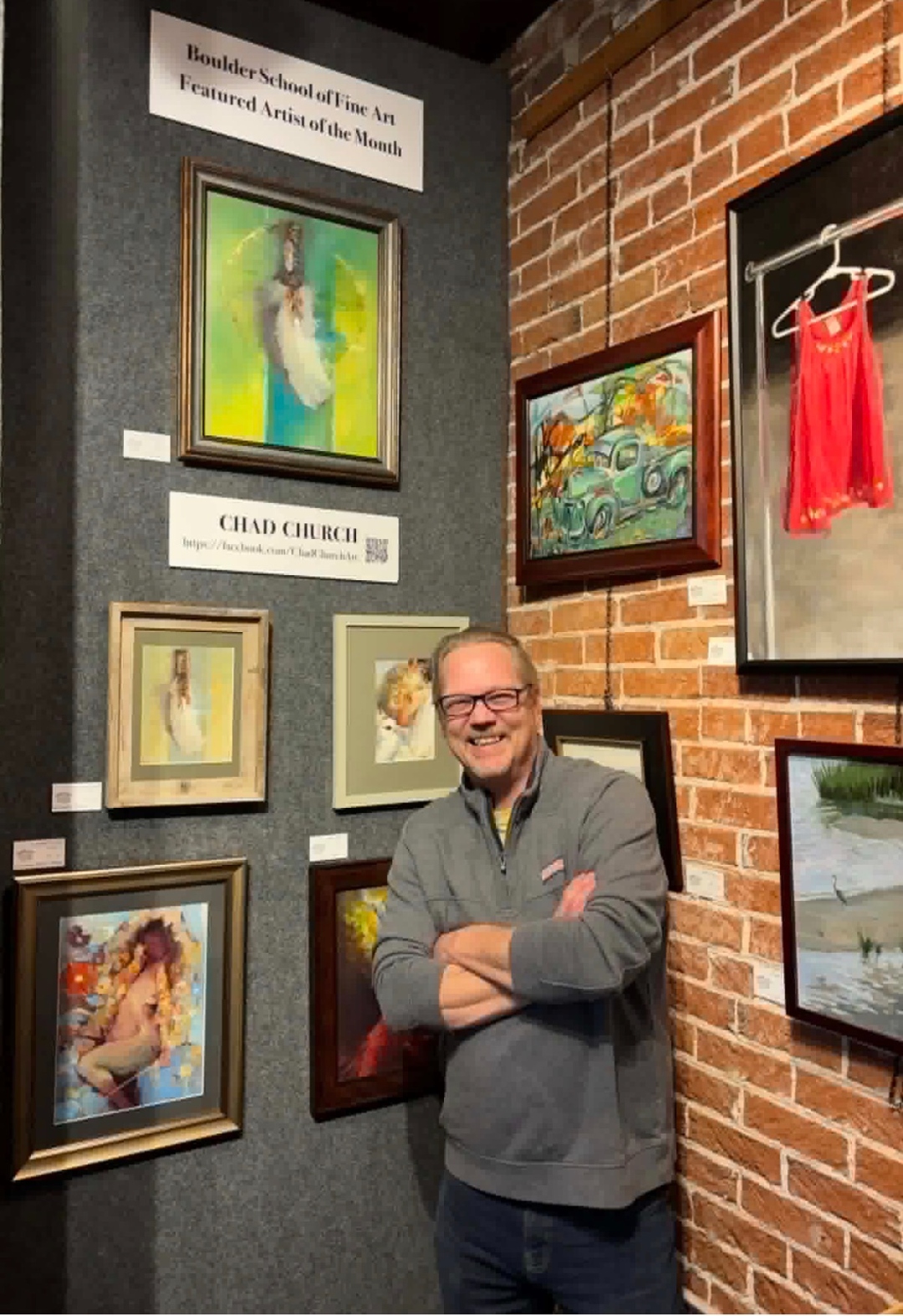 Chad Church standing with arms crossed in front of his artwork at the Boulder School of Fine Art Featured Artist of the Month display